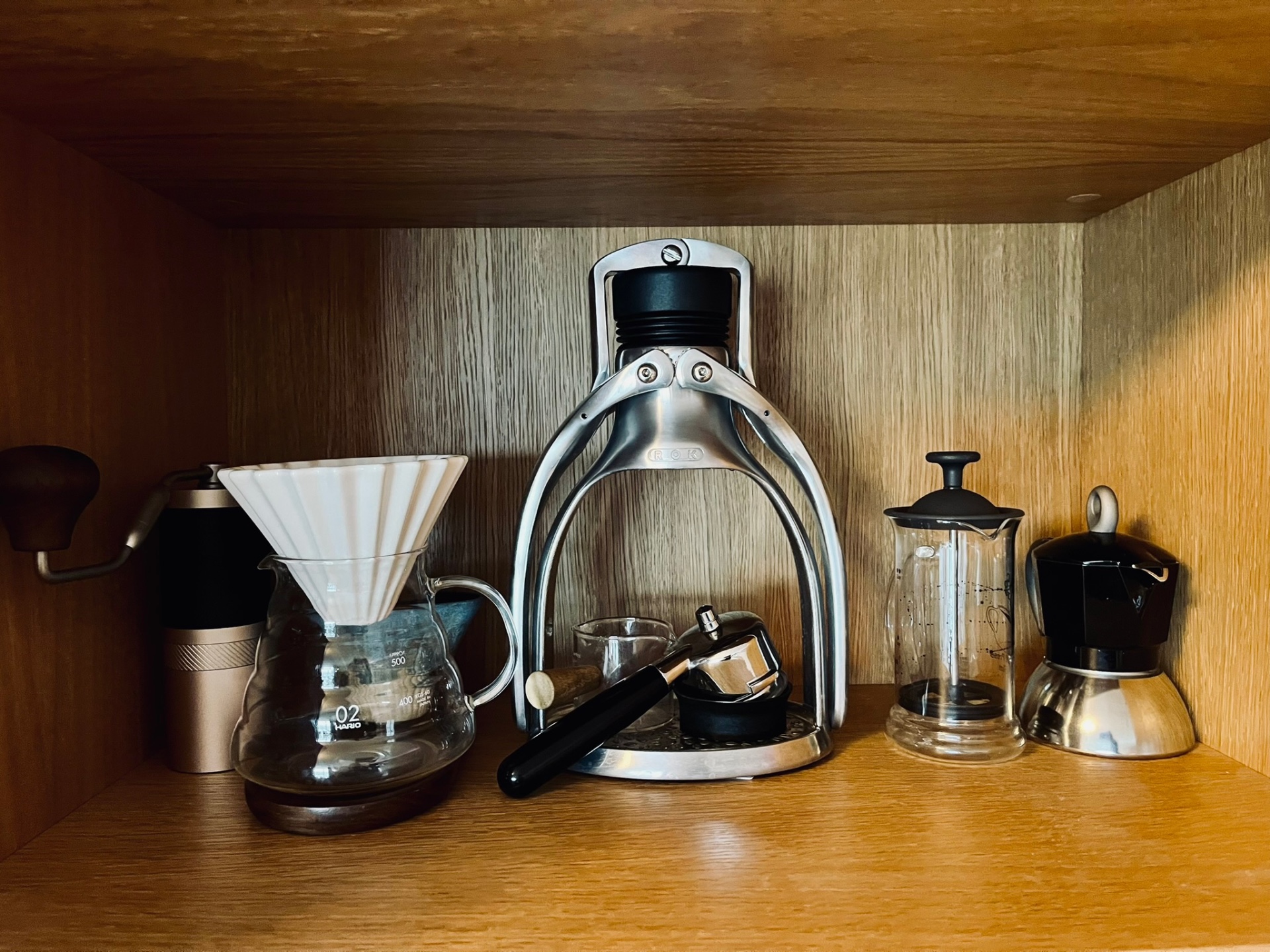A shelf with hand grinder, Hario V60, ROK espresso maker, plunger and moka pot