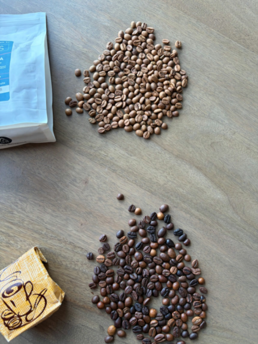 Two piles of coffee beans on a wooden surface — light roast beside a darker roast